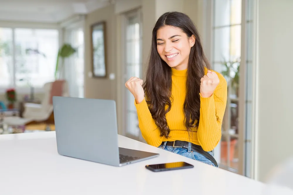 Smiling woman celebrating in front of a laptop